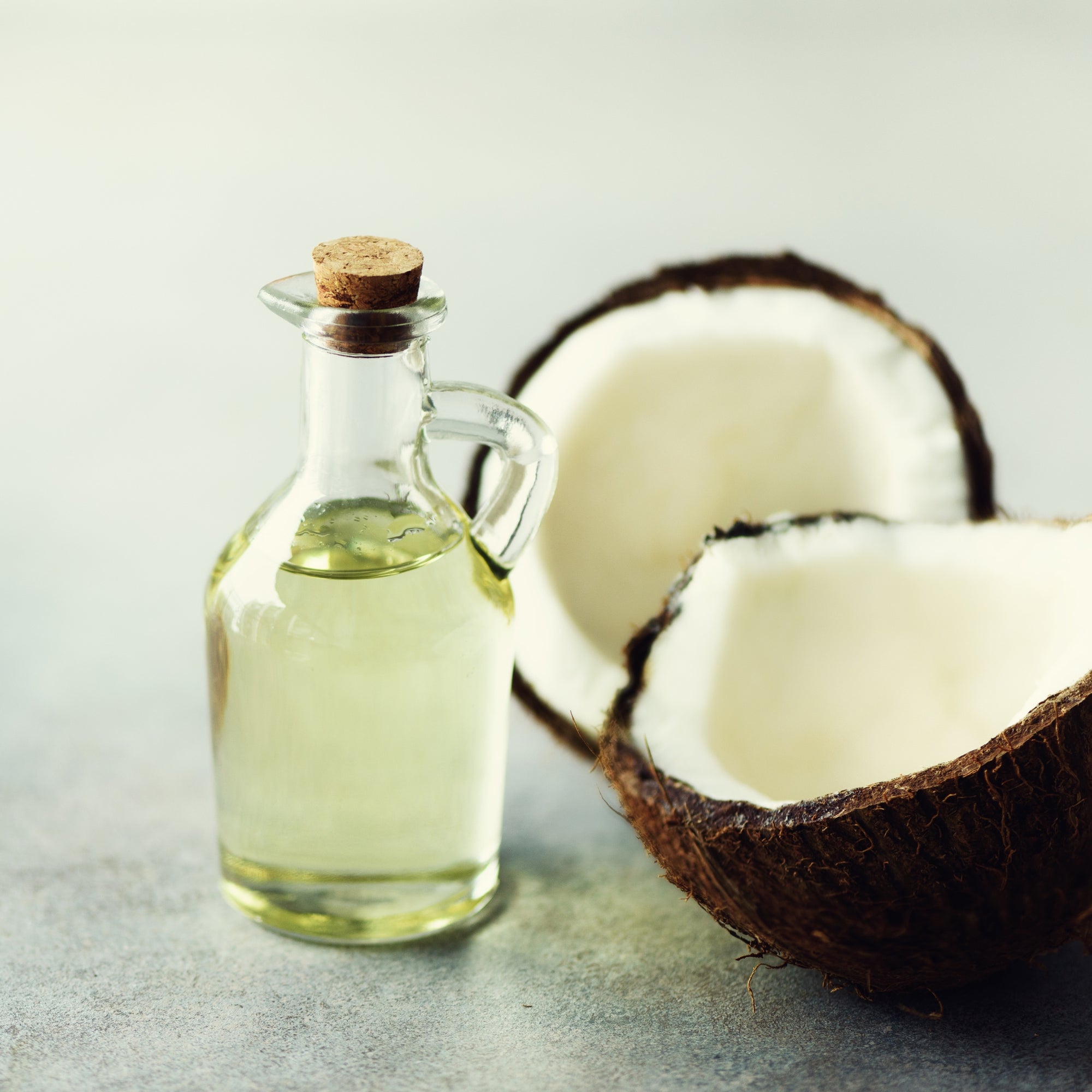 Cracked two halves of fresh organic coconut and coconut oil on grey background