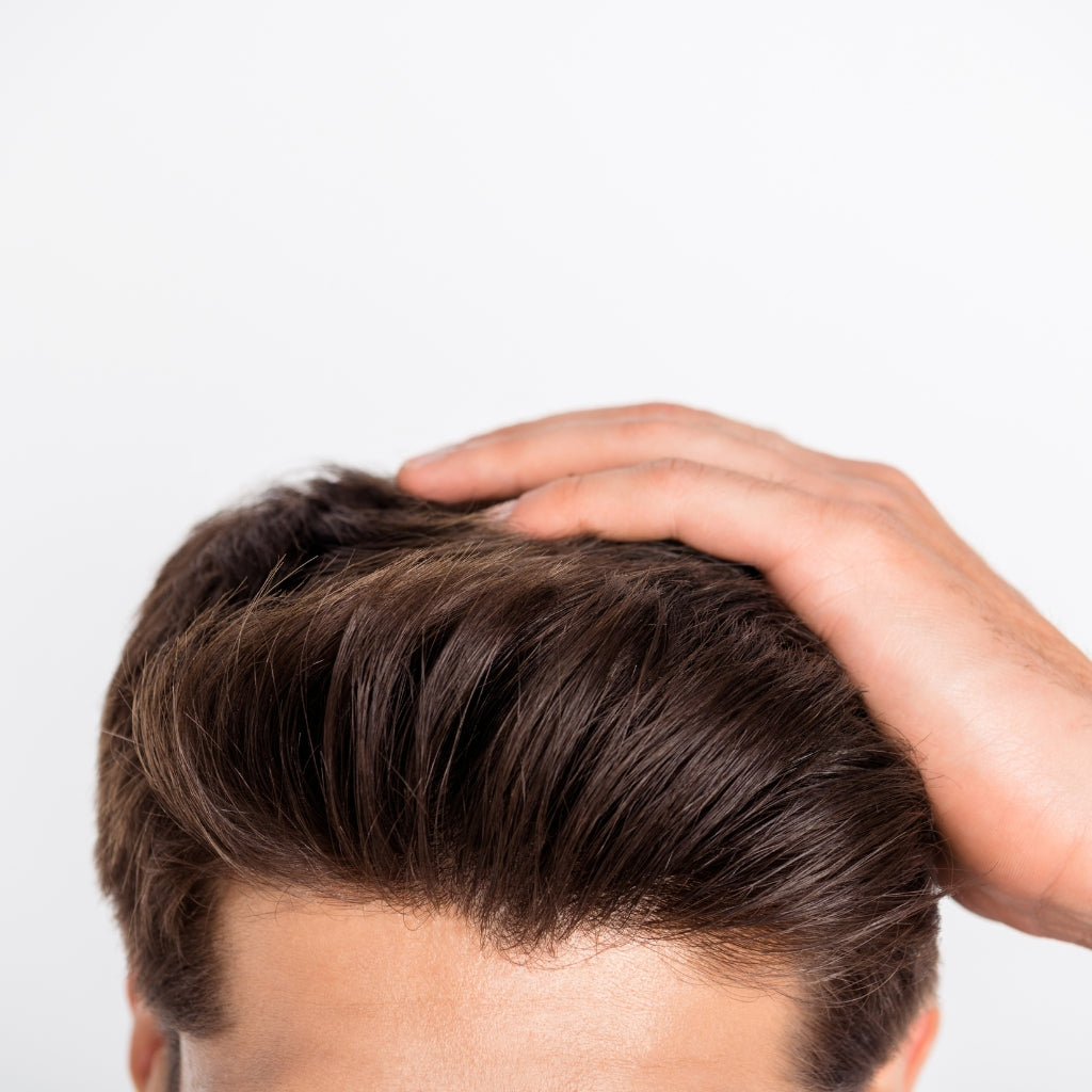 A young adult man with normal hair, running his fingers through his voluminous and conditioned hair, demonstrating the effective results of using &Better's all-natural shampoo bar.