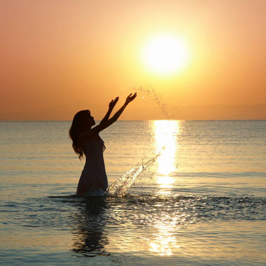 Sunset on the beach next to the ocean white dressed long hair beautiful lady splashing water