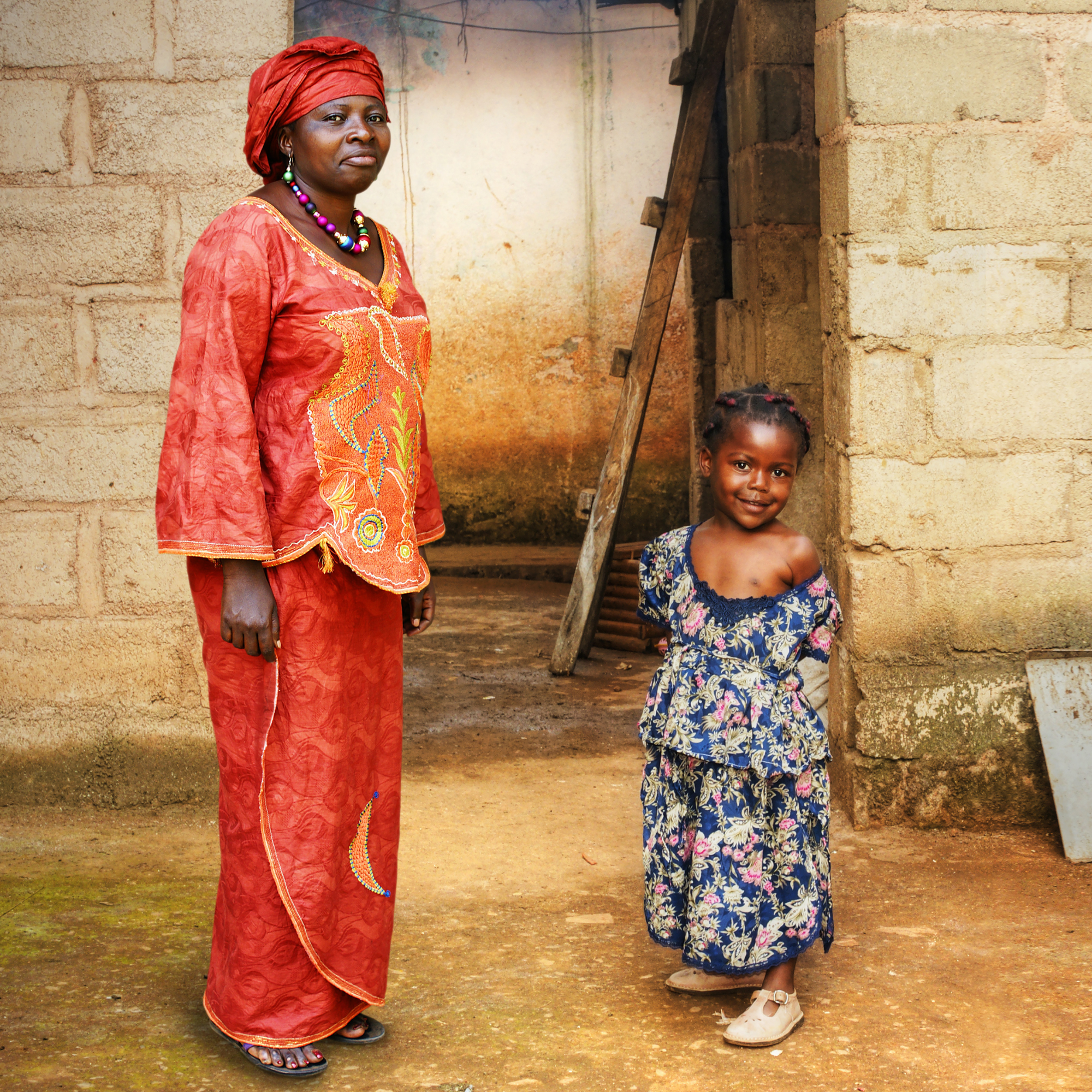 An African woman, dressed in traditional attire, and her child standing together in a rural African village, embodying a sense of culture, heritage, and familial warmth