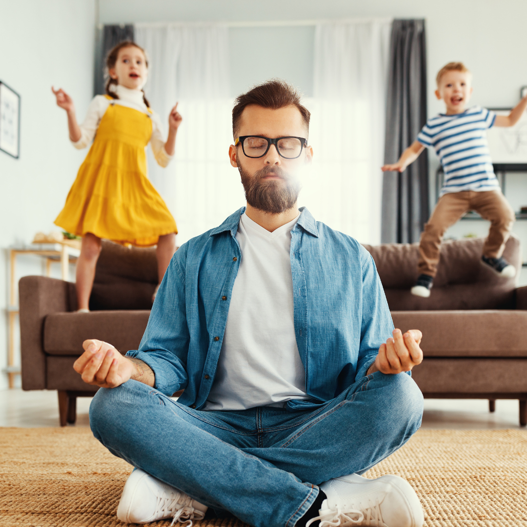 A young father practicing mindfulness meditation, sitting peacefully with closed eyes, while his children play joyfully in the background.