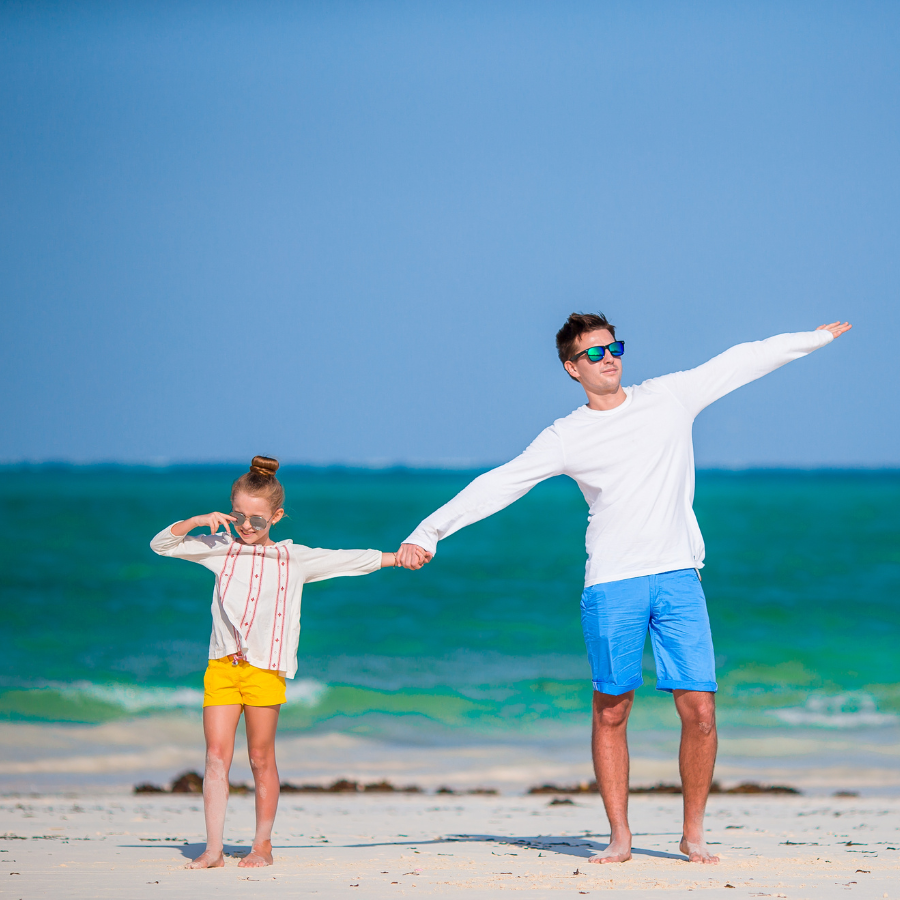 A father and child holding hands in a beach, representing the connection between eco-friendly personal care choices and setting a positive example for future generations.